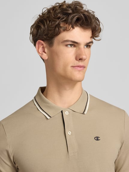 Männermodel trägt Slim Fit Poloshirt mit Label-Stitching von CHAMPION in Beige, Reine Baumwolle, Knopfleiste, Nahaufnahme Oberkörper. Rückenlänge bei Größe M: 73 cm.