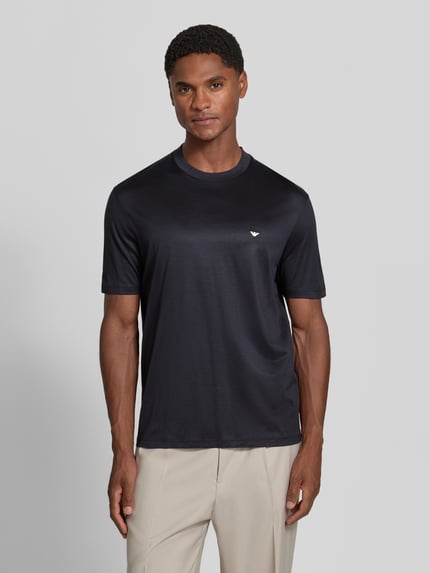 Männermodel trägt T-Shirt aus Lyocell-Mix mit Label-Stitching von Emporio Armani, schwarz, dezenter Glanz, taillierte Passform, Ganzkörperansicht von vorne.