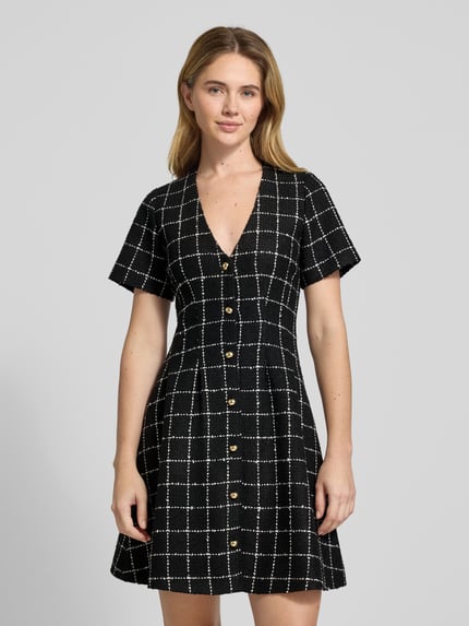 Vrouwenmodel draagt Tailliertes Etuikleid met Gitterkaro-Muster Modell 'KIKLA' van HUGO, zwart-wit, bouclé, V-hals, knielang, korte mouwen, allover ruitpatroon, knoopsluiting, getailleerd, voorkant bovenlichaam close-up.