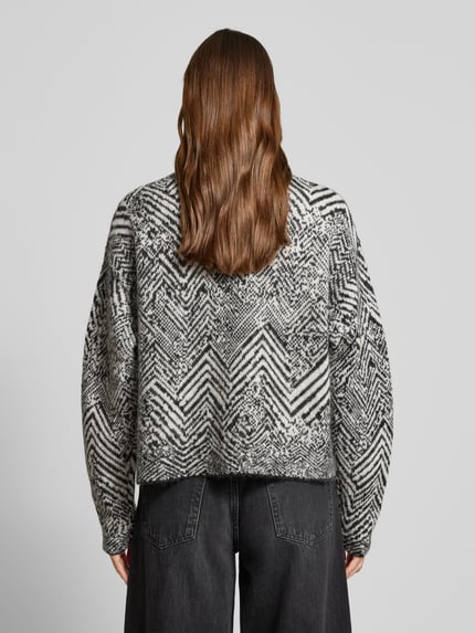 Vrouwenmodel draagt Oversized Strickpullover aus Mohair-Woll-Mix Modell 'FACLINA' van BOSS met zwart-wit jacquard all-over patroon, asymmetrische zoom, lange mouwen, mock neck, grof gebreide textuur, geheel van achteren bekeken.