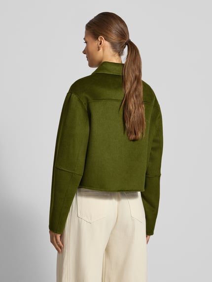 Frauenmodel trägt kurz geschnittene, olivgrüne Jacke aus Lanawoll-Mix mit Knopfleiste Modell 'ALEX' von MANGO, matte Textur, Ganzkörperansicht Rückansicht, Regular Fit, Umlegekragen, Damen Jacke mit Viskose-Anteil.