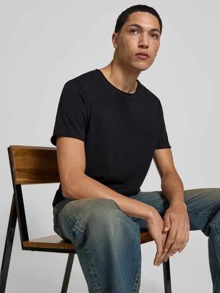 Męski model nosi T-Shirt mit Rollsaum od Filippa K, czarna bawełna, prosty krój, okrągły dekolt, długość tyłu 70 cm w rozmiarze M, zdjęcie w ujęciu na górną część ciała z przodu.