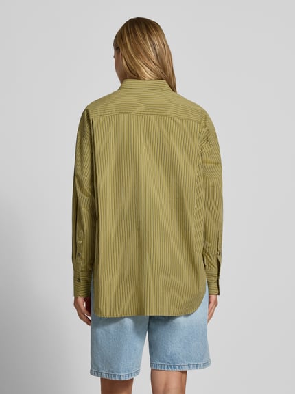 Männermodel trägt bluzka koszulowa Relaxed Fit Hemdbluse aus reiner Baumwolle Modell 'JAMIE' von JJXX, w odcieniach oliwkowej zieleni i żółci, cienkie paski, kołnierzyk koszulowy, długi rękaw, brustasza, listwa guzikowa, szerokie ramiona, długość tyłu 77 cm w rozmiarze S, długość rękawa 56 cm w rozmiarze S, widok całej sylwetki od tyłu