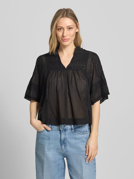 Frauenmodel trägt Blusenshirt mit V-Ausschnitt Modell 'Siama' von Neo Noir in Schwarz mit Stitchings, Regular-Fit, Ganzkörperansicht von vorne. Rückenlänge bei Größe 36: 56 cm, Ärmellänge bei Größe 36: 28 cm.