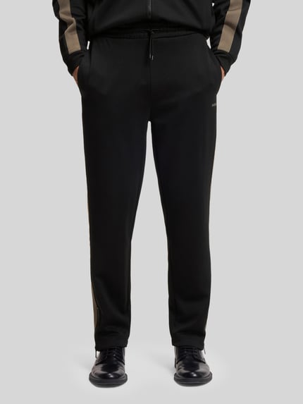 Männermodel trägt Relaxed Fit Jogginghose mit Galonstreifen Modell 'DOLOS' von HUGO, unifarben, Sweatmaterial, seitliche Eingrifftaschen, Nahaufnahme Vorderansicht.