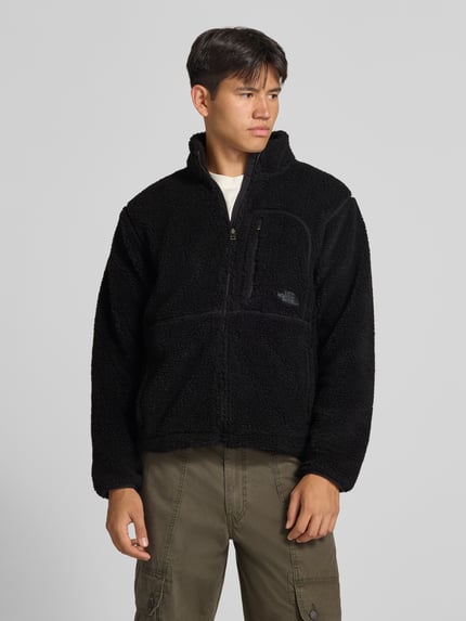 Männermodel trägt schwarze Fleecejacke mit Stehkragen und Brusttasche Modell 'EXTREME PILE' von The North Face, Teddyfellstruktur, Reißverschluss, Label-Stitching, Regular Fit, Ganzkörperansicht von vorne.