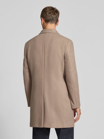 Mannenmodel draagt Relaxed Fit Mantel uit zuiver katoen model ‘AMSTERDAM‘ van MCNEAL, beige, reverskraag, knoopsluiting, geheel achteraanzicht.