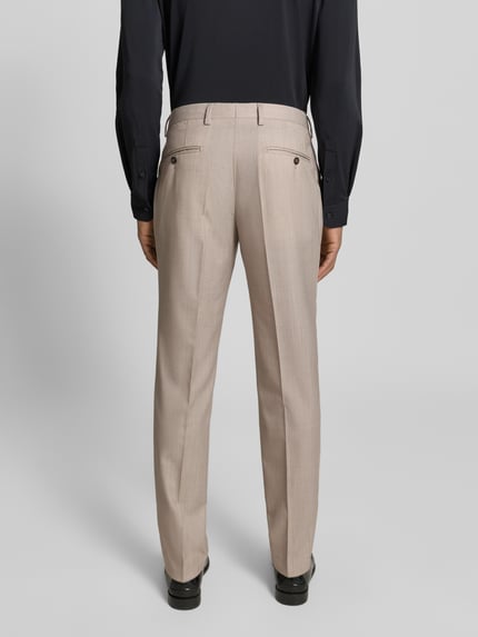 Männermodel trägt Anzughose aus Schafswoll-Mix Modell 'Ryan' von Pierre Cardin in Beige mit Bügelfalten, Ganzkörperansicht Rückansicht. Slim Fit, Gesäßtaschen, Bundweite 38 cm, Innenbeinlänge 81 cm.