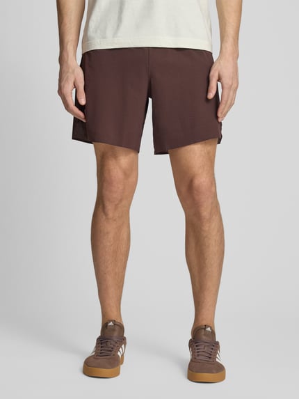 Männermodel trägt Shorts mit elastischem Logo-Bund Modell 'SENSE AERO' von Salomon aus Material-Mix mit Stretch-Anteil in Braun, Loose-Fit, Logo-Print, Ganzkörperansicht von vorne. Bundweite 38 cm, Innenbeinlänge 18 cm, Größe M.