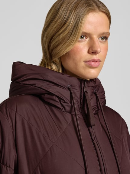 Frauenmodel trägt Relaxed Fit Steppmantel mit Kapuze von Marc O'Polo in dunklem Braun mit leichtem Glanz, Nahaufnahme Oberkörper. Damen Steppmantel von Marc O'Polo DENIM