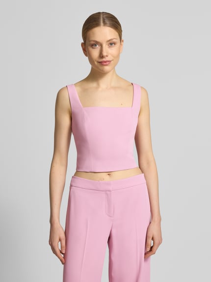 Frauenmodel trägt Cropped Top mit Karree-Ausschnitt und rückseitigem Reißverschluss von Jake*s Cocktail in Rosa, körpernaher Schnitt, Material-Mix, leicht glänzende Textur, Ganzkörperansicht von vorne.