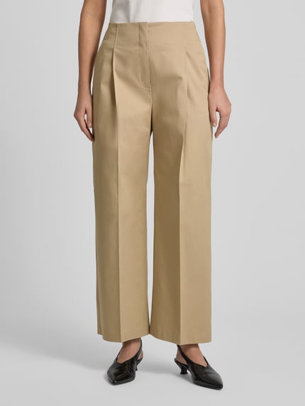 Vrouwenmodel draagt Straight Leg Bundfaltenhose aus Baumwoll-Mix Modell 'TULOTTA' van BOSS, beige katoenmix, wide leg, high waist, label detail, ingestikte vouwen, zijzakken, voorkant volledig zichtbaar, close-up op onderlichaam.