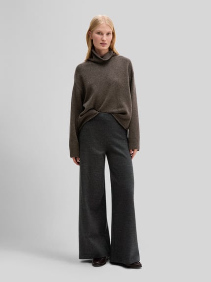 Frauenmodel trägt Rollkragenpullover mit überschnittenen Schultern von MARC O'POLO in unifarbener Strickoptik, Ganzkörperansicht von vorne.