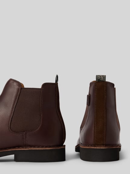 Produktfoto, Chelsea Boots aus Rindsleder mit Logo-Detail von POLO RALPH LAUREN in Dunkelbraun mit Struktur in Lederoptik, unifarben, seitliche Stretcheinsätze, Applikation, sichtbare Nähte und profilierter Gummisohle, flache Absatzform, Rückansicht.