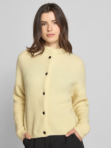 Vrouwenmodel draagt Regular Fit Cardigan uit alpaka-mix model 'Alpha' van Gestuz, elastisch materiaal, opstaande kraag, knoopsluiting, gebreide textuur, lengte rug 55 cm, mouwlengte 48 cm, kleur zachtgeel, voorkant, halve lichaamsopname.