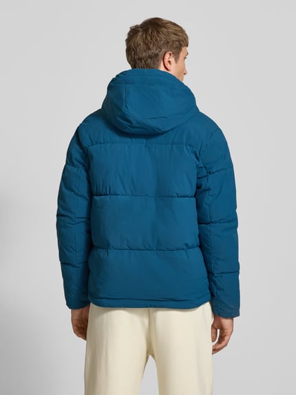 Męski model nosi kurtkę pikowaną z kapturem Model 'GALAXY' od JACK & JONES w kolorze niebieskim, krój regular fit, wpuszczane kieszenie, zamek błyskawiczny, długość tyłu w rozmiarze M: 70 cm, szerokość ramion w rozmiarze M: 49 cm, szerokość w rozmiarze M: 58 cm, długość rękawów w rozmiarze M: 69 cm, widok całej sylwetki z tyłu