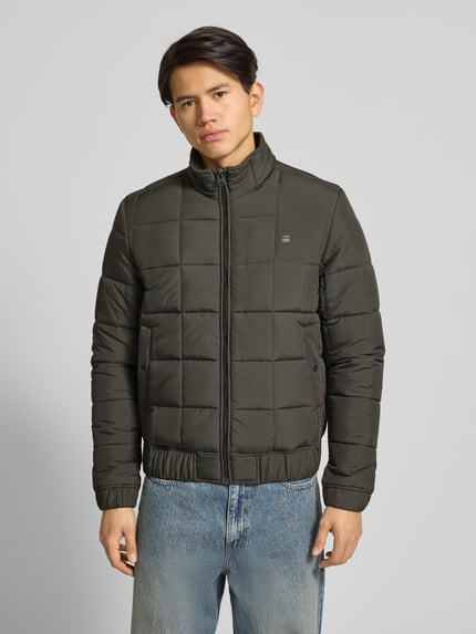 Männermodel trägt Steppjacke mit Reißverschluss von G-Star in Olivgrün, Regular Fit, Stehkragen, Label-Print, Eingrifftaschen, elastische Abschlüsse, Ganzkörperansicht von vorne. Rückenlänge bei Größe M: 68 cm, Schulterbreite: 46 cm, Brustweite: 41 cm, Ärmellänge: 71 cm.
