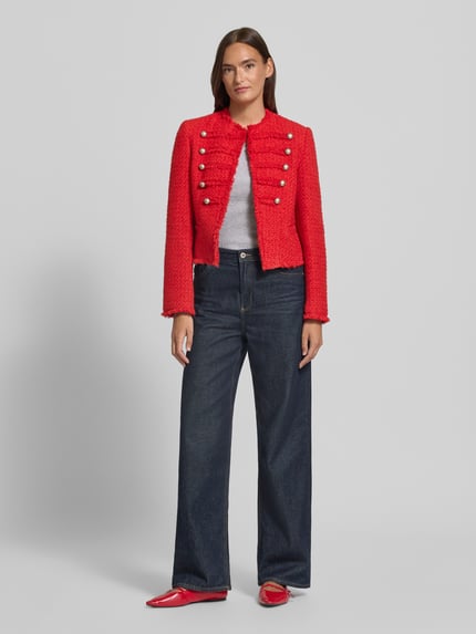 Frauenmodel trägt Blazer in Bouclé-Optik Modell 'CAROLINA' von MANGO in Rot mit Zierknöpfen, Fransensaum und Rundhalsausschnitt, Ganzkörperansicht von vorne. Baumwoll-Mix, Straight Fit, Hakenverschluss, kombinierbar zu Jeans und Schuhen.