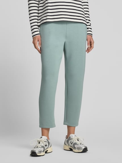 Frauenmodel trägt Cropped Sweatpants mit elastischem Bund und Eingrifftaschen von Christian Berg Woman aus grünem Modal-Mix, Ganzkörperansicht von vorne.