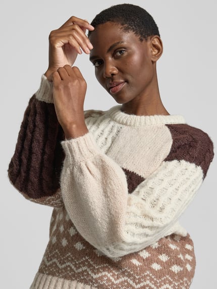 Frauenmodel trägt Pullover mit Strukturmix von VERO MODA in Creme, Braun und Beige mit Patchwork, Zopf- und Punktmuster, Nahaufnahme Oberkörper.