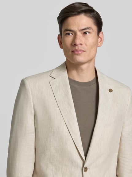 Männermodel trägt Regular Fit Sakko aus reinen Leinen mit Reverskragen von Christian Berg Men in hellem Beige, Nahaufnahme Oberkörper. Rückenlänge 75 cm, Schulterbreite 47 cm, Ärmellänge 63 cm, Reverskragen, Brusttasche, AufgesetzteTaschen, 2-Knopfleiste.