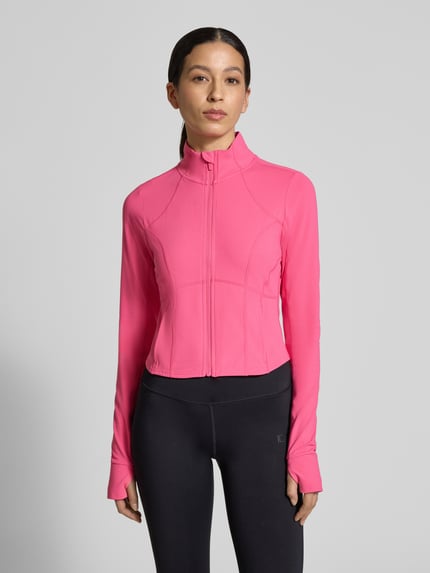 Frauenmodel trägt Slim Fit Jacke mit Stehkragen Modell 'Storm' von Fabletics in Pink, Crop Fit, Daumenschlaufen, Ganzkörperansicht von vorne.