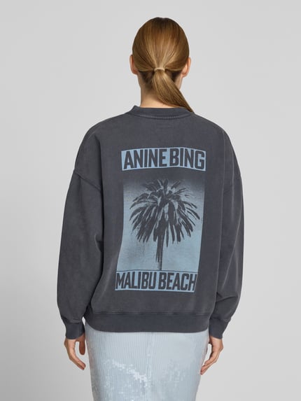 Kobiece model prezentuje Regular Fit Sweatshirt mit Logo-Print od Anine Bing, czarny z niebieskim nadrukiem, czysta bawełna, krój regular fit, elastyczne wykończenia, długość pleców w rozmiarze S: 62 cm, widok całej sylwetki od tyłu.