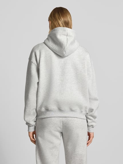 Frauenmodel trägt Relaxed Fit Hoodie aus Baumwoll-Mix Modell 'Iconic' von Gina Tricot, hellgrau, weiche Textur, Ganzkörperansicht Rückansicht. Damen Hoodie von Gina Tricot, Baumwoll-Mix, Relaxed Fit, Känguru-Tasche, elastische Abschlüsse.