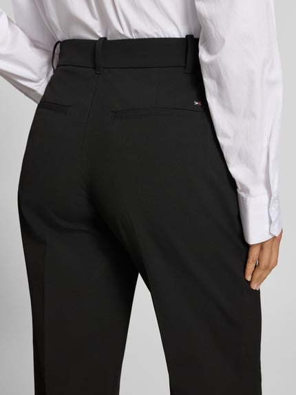 Frauenmodel trägt Regular Fit Schlaghose mit Bügelfalten von Tommy Hilfiger in einfarbigem Schwarz, mit Bundfalte, Gesäßtaschen und Gürtelschlaufen, Nahaufnahme Rückansicht.