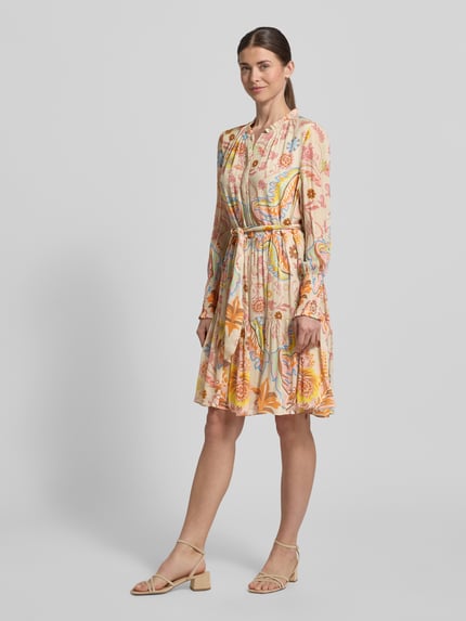 Vrouwenmodel draagt Regular Fit jurk met bloemen all-over print van HERZENS, getailleerd, opstaande kraag, knoopsluiting, met lange mouwen, afneembare stoffen band, ruglengte maat 36: 97 cm, borstwijdte: 52 cm, mouwlengte: 65 cm, lichte kleuren, ronde vormen, gladde textuur. Ganzkörperansicht van voren.