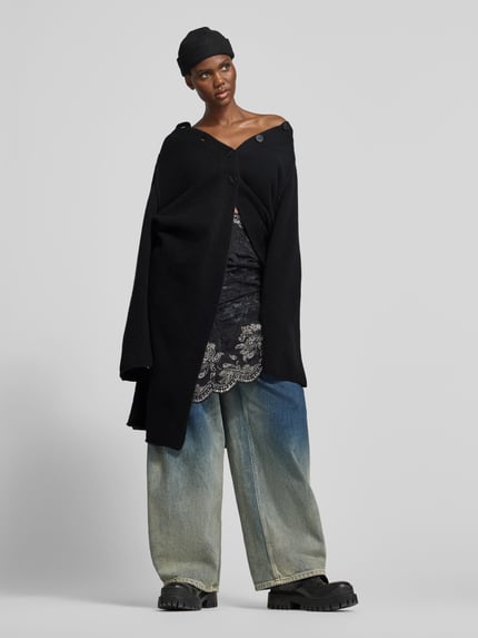 Frauenmodel trägt Funktionsjacke mit einreihiger Knopfleiste von black palms, melierte Optik, strukturierte Strick-Textur, longline, schwarze Farbe, Ganzkörperansicht von vorne.