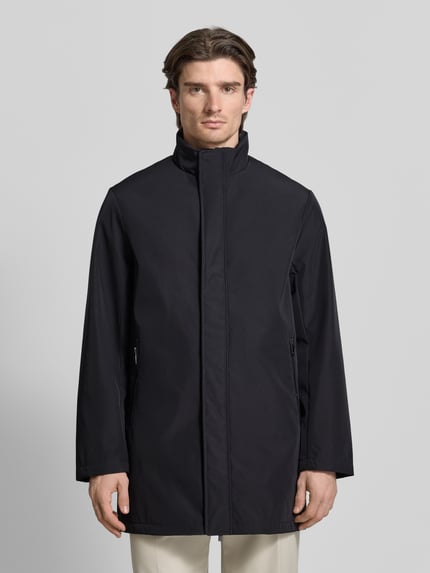 Männermodel trägt Trenchcoat mit Stehkragen von ARMANI EXCHANGE in Schwarz, gerader Schnitt, verdeckter Reißverschluss, Ganzkörperansicht von vorne.