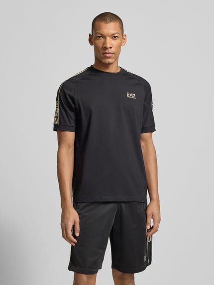Männermodel trägt T-Shirt aus Viskose-Mix mit Logo von EA7 Emporio Armani, Regular-Fit, Rundhalsausschnitt, Schwarz, Ganzkörperansicht von vorne.