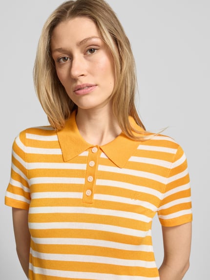 Vrouwenmodel draagt 'Regular Fit Poloshirt aus Lyocell-Seiden-Mix' van Tommy Hilfiger met allover-streepjesmotief, fijngebreid, polokraag, korte knoopsluiting, korte mouwen met geribde zoom, logo-stitching, regular fit; geel-wit, zachte textuur. Close-up bovenlichaam.