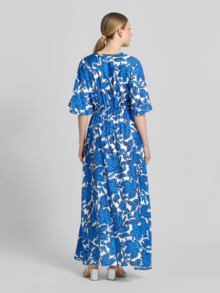 Vrouwenmodel draagt dames maxi-jurk van viscosemix met blauwe en witte bloemen, getailleerd model, trekkoord, model 'KAIA' van B.Young, ruglengte maat 36: 35 cm, borstwijdte 44 cm, mouwlengte 31 cm, volledig van achteren te zien.