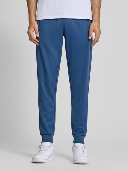 Männermodel trägt Sweatpants mit elastischem Bund Modell 'BERTONI' von Ellesse aus Baumwoll-Mix, Regular-Fit, Label-Detail, Ganzkörperansicht von vorne.