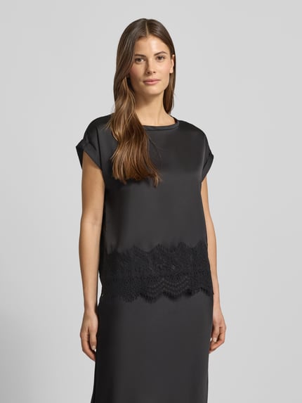Modelka nosi T-Shirt z okrągłym dekoltem model 'ELLETTE' od Vila, luźny fason, koronka, satyna, długość pleców w rozmiarze 36: 59 cm, ujęcie całej sylwetki z przodu.