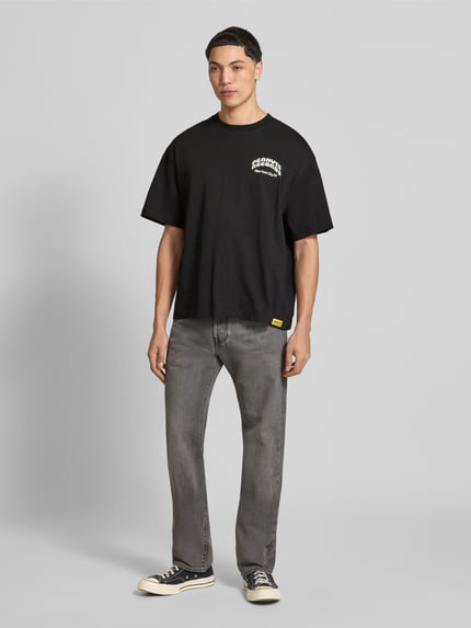 Mannenmodel draagt Regular Fit T-Shirt uit zuivere katoen model 'PEANUTS' van Only & Sons, Peanuts® print, jersey, ronde hals, korte mouw, zwart, grijze jeans, frontale volledige lichaamsweergave.