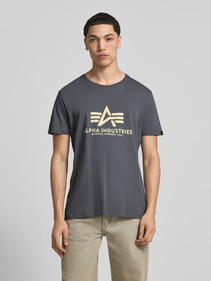 Männermodel trägt T-Shirt mit Label-Detail Modell 'BASIC' von Alpha Industries in Grau, Reine Baumwolle, Gerader-Schnitt, Rundhalsausschnitt, Rückenlänge bei Größe M: 69 cm, Ganzkörperansicht von vorne.