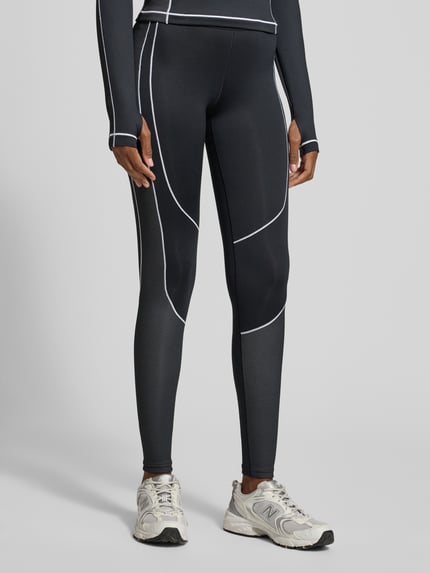 Kobiece model prezentuje Legginsy mit elastischem Logo-Bund od Under Armour, czarne z białymi przeszyciami, dopasowany krój, elastyczna mieszanka materiałów z dodatkiem streczu, widok z przodu, ujęcie całej sylwetki.