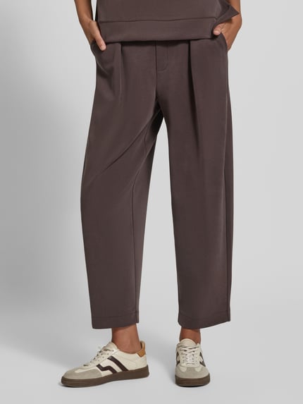 Frauenmodel trägt Sweatpants aus Modal-Mix mit Bundfalten von Rich & Royal, dunkler Braunton, Barrel Fit, elastischer Bund, Nahaufnahme Unterkörper.