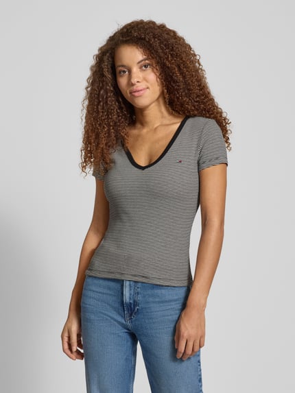 Modelka kobieca nosi Slim Fit T-Shirt aus Baumwoll-Mix od Tommy Jeans, szary, prążkowany, logo, dekolt V, krótkie rękawy, ujęcie całej sylwetki z przodu.