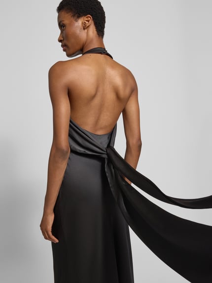 Vrouwenmodel draagt avondjurk met Viskose-Anteil van Forever New in zwart satijn met sierknoop en sleep, nauwsluitend Materiaalmix, Maxilengte, mouwloos design, halter met haakjessluiting, Ganzlichaamsaanzicht Rückansicht.