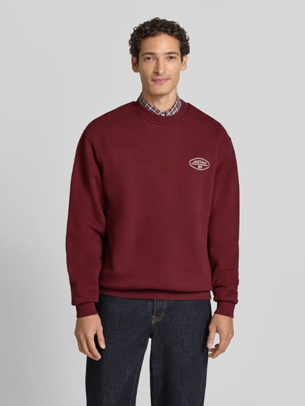 Männermodel trägt Sweatshirt mit Logo-Print Modell 'Worldwide' von Les Deux in Dunkelrot, Baumwoll-Mix, Ganzkörperansicht von vorne.