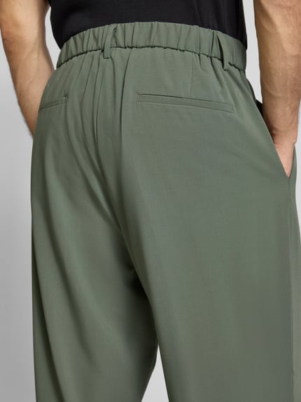 Männermodel trägt Stoffhose mit Label-Detail von Antony Morato in Oliv, Material-Mix mit Viskose-Anteil, Gesäßtaschen, Nahaufnahme Rückansicht.