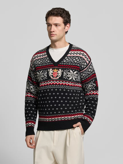Männermodel trägt Pullover aus Wolle mit Wappenstickerei von POLO RALPH LAUREN, mehrfarbiges Jacquardmuster, V-Ausschnitt, Ganzkörperansicht von vorne.