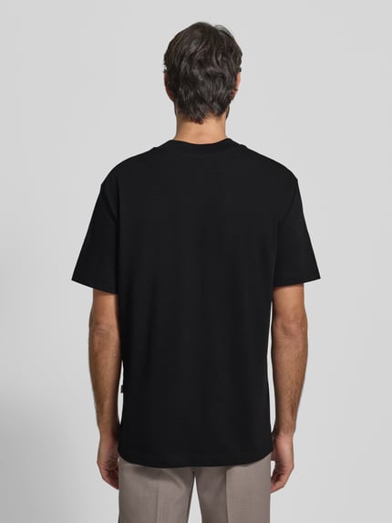 Männermodel trägt Regular Fit T-Shirt aus reiner Baumwolle Modell 'COLMAN' von SELECTED HOMME in Schwarz, Ganzkörperansicht Rückansicht. Unifarbene Optik, Rundhalsausschnitt, kurze Ärmel, lässiger Schnitt, Größe M: Rückenlänge 71 cm, Brustweite 56 cm.