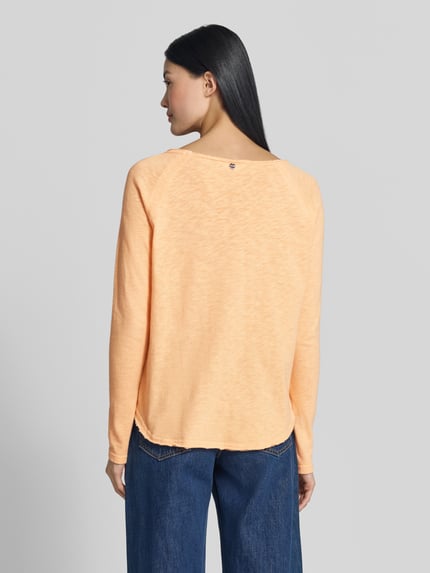 Frauenmodel trägt Langarmshirt aus reiner Baumwolle mit Raglanärmeln von Rich & Royal in zartem Orange, taillierte Passform, Rundhalsausschnitt, Rückenlänge bei Größe S: 60 cm, glatte Struktur, Ganzkörperansicht Rückansicht.