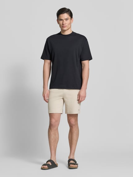 Męski model nosi Regular Fit Sweatshorts aus Baumwoll-Mix Modell 'AUSTIN' od HUGO, jasny beżowy kolor, wafelowa faktura, boczne kieszenie, elastyczny pas z troczkiem, krój regular fit, widok całej sylwetki z przodu.