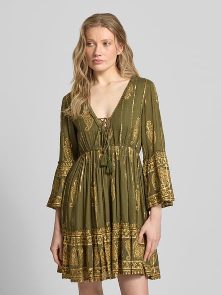 Frauenmodel trägt Minikleid aus Viskose-Mix mit Schnürung von Apricot, olivgrün mit goldenen Mustern, A-Linie, V-Ausschnitt, Trompetenärmel, Nahaufnahme Oberkörper.